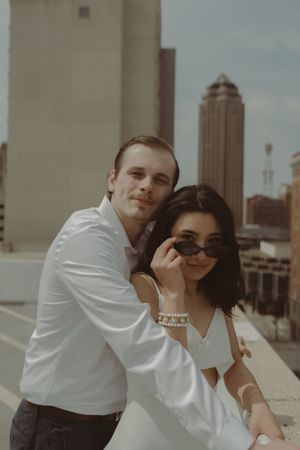 A stylish couple poses on a rooftop with downtown Des Moines architecture in the background.