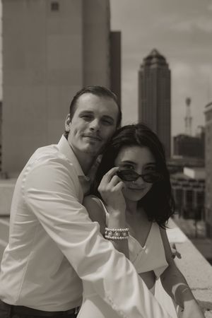 A couple shares an intimate moment on an urban rooftop with sunglasses and matching white outfits.