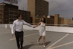 A couple in white outfits dances together on an urban rooftop parking deck.