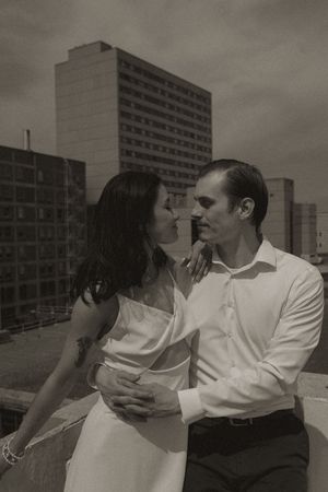 Romantic couple in white and dark clothing share an intimate moment on a city rooftop.