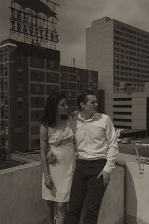 Two people lean against a concrete wall on an urban rooftop with buildings in view.