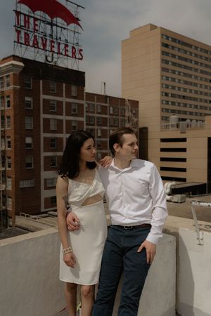 Couple in coordinated outfits pose together against an urban rooftop backdrop.