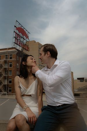 Two people share affectionate moments while sitting on a concrete ledge of a city building.