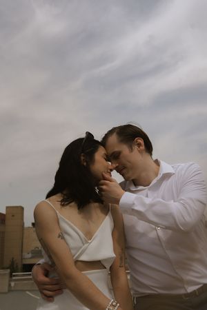 A couple embraces on an urban rooftop, with dramatic cloudy skies in the background.