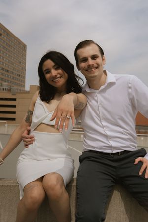 A couple in contrasting white and dark outfits shares playful moments on a rooftop setting.