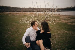 Two people share intimate moments near blooming branches in a rustic outdoor setting.