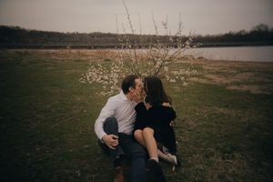A couple embraces near flowering branches in a serene outdoor landscape.