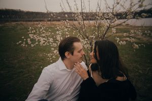 Two people share tender moments near spring blossoms in a natural setting.