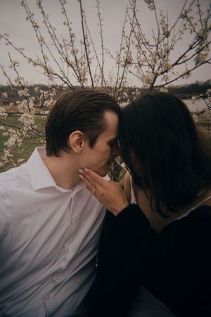 Tender moment between couple beneath flowering branches in moody lighting.