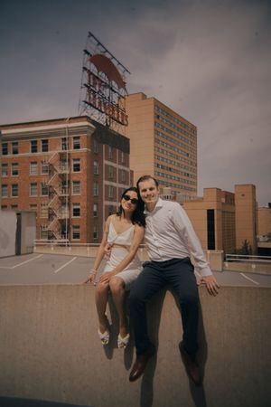Couple posing playfully on rooftop with urban buildings in background.