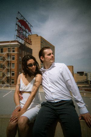 Dynamic shot of couple leaning back on rooftop with cityscape behind them.
