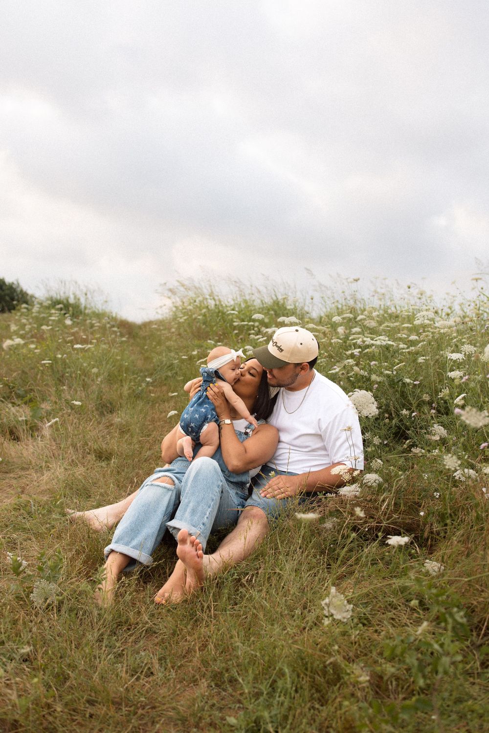 A couple relaxes together in a meadow filled with white wildflowers on a cloudy summer day.