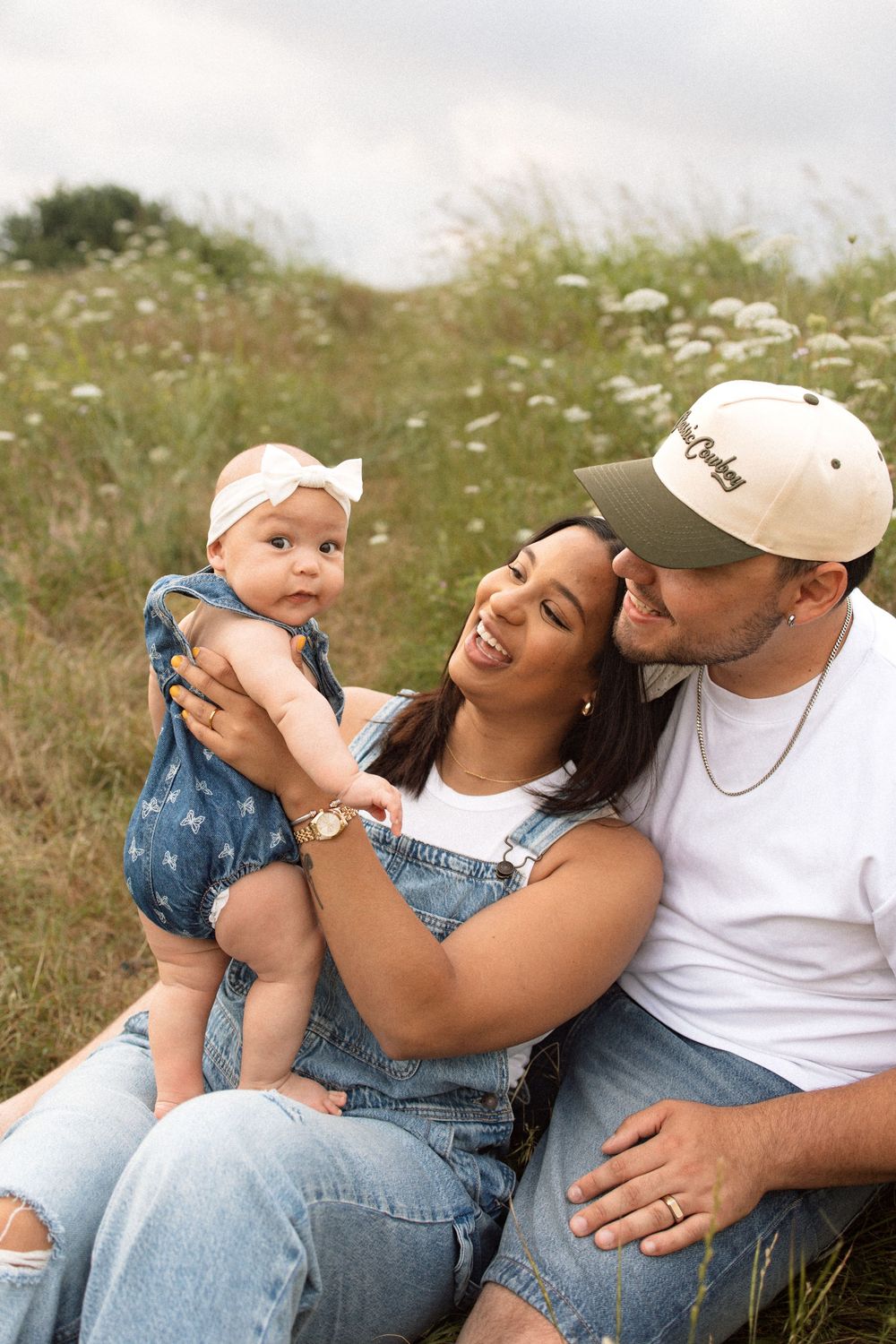 A happy family sits together in a wildflower meadow wearing matching denim on a sunny summer day.
