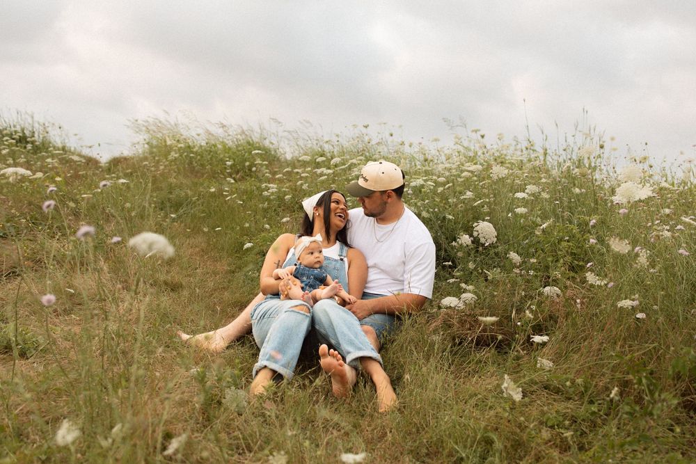 A couple and child sit together in a wildflower meadow on a warm summer day.