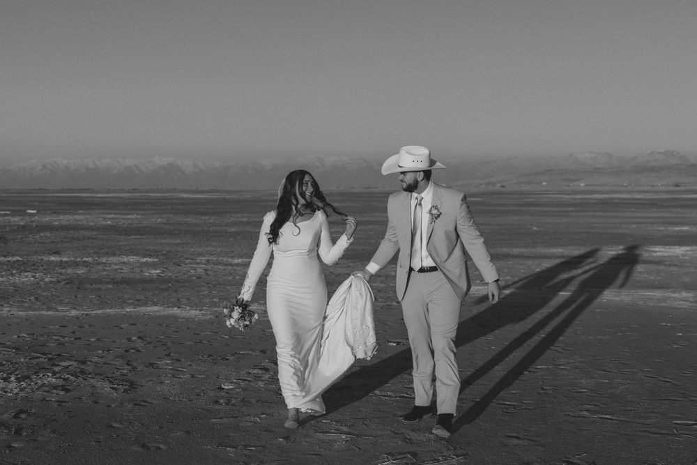 Couple walking hand in hand along a beach in black and white.