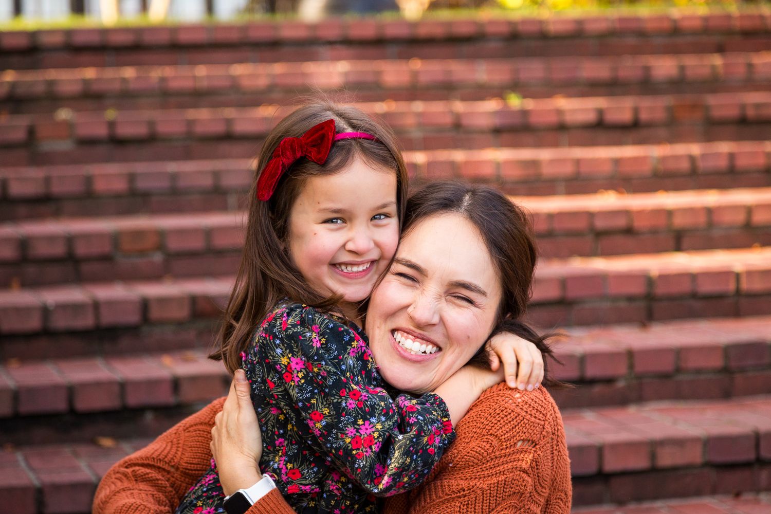 Two people embrace and smile warmly while sitting on outdoor brick steps.