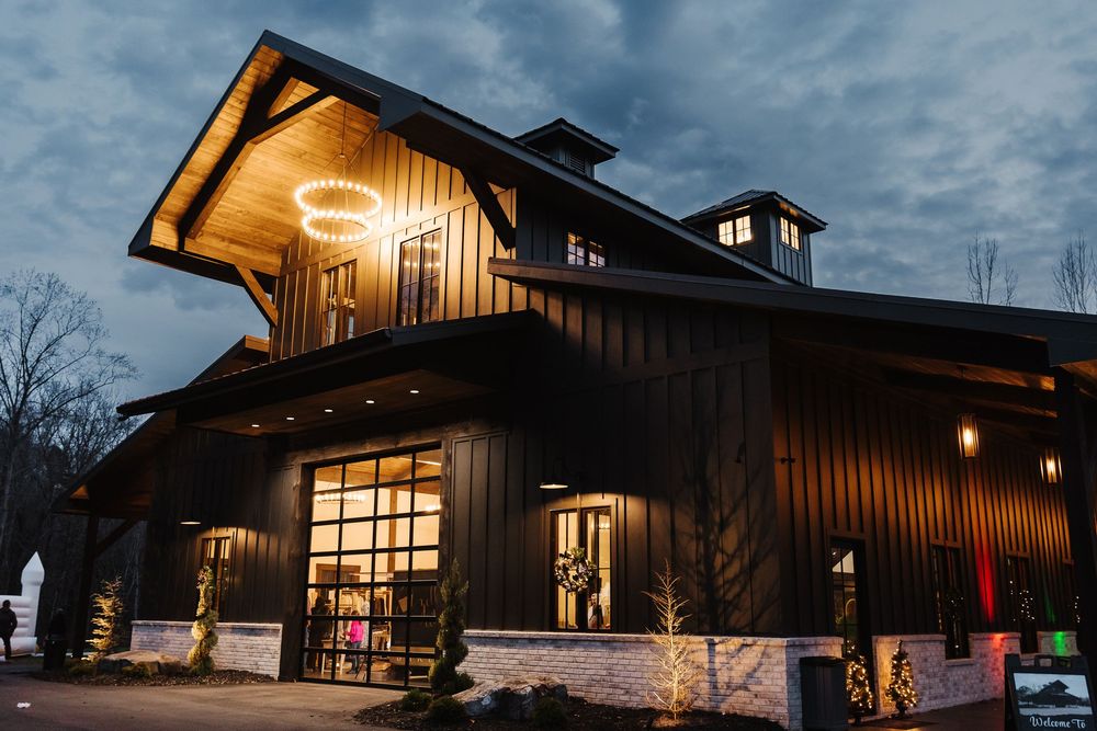Modern mountain lodge with wood siding and large windows illuminated at dusk against a moody blue sky.
