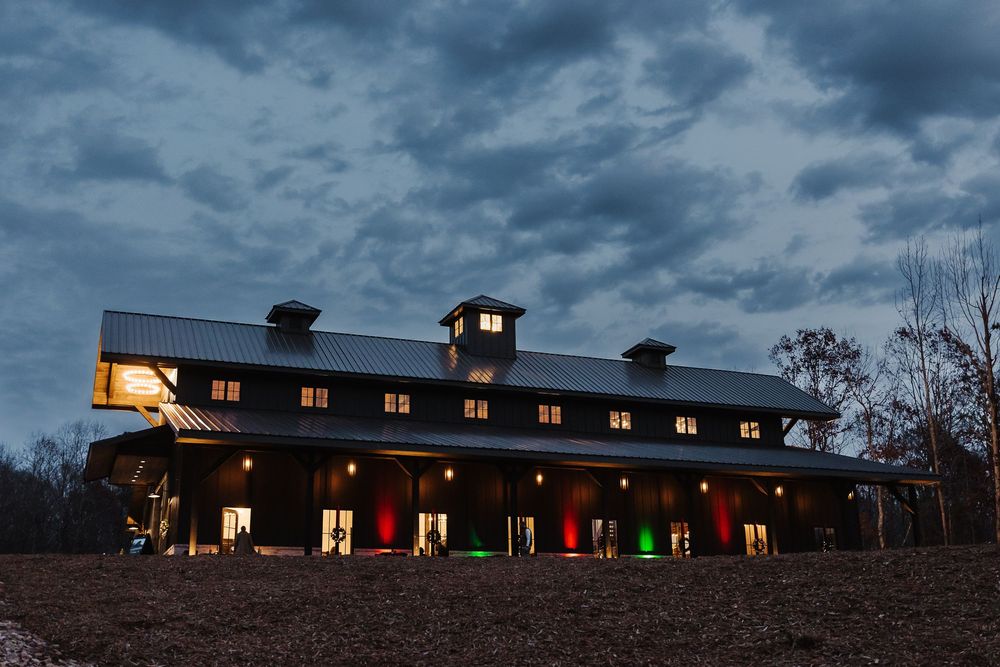 A rustic barn with glowing multicolored garage doors illuminated at dusk under dramatic cloudy skies.