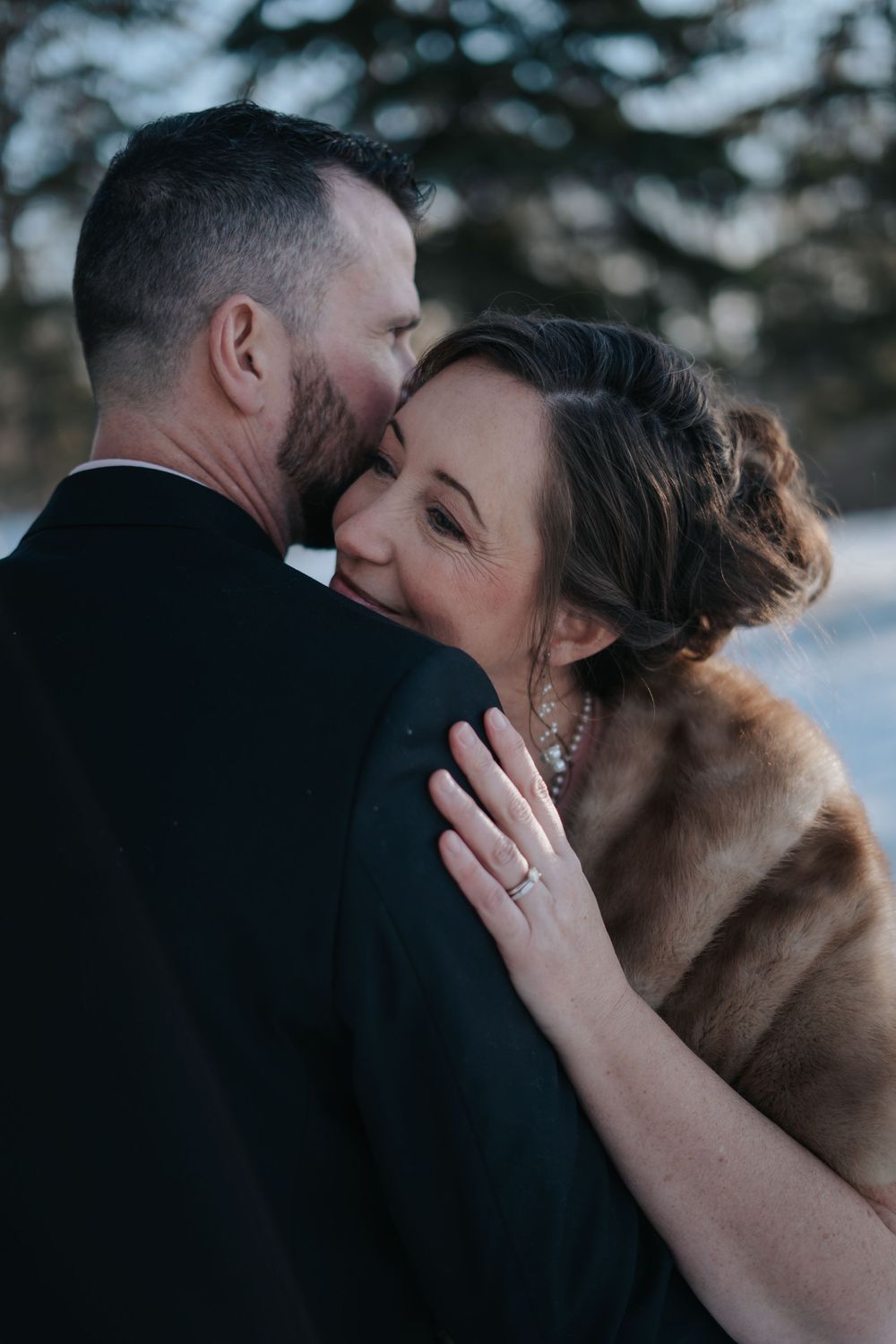 Romantic winter wedding photo of couple embracing in formal attire.
