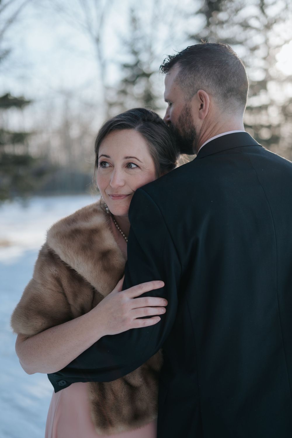 Intimate moment between newlyweds in winter setting with snow-covered trees.
