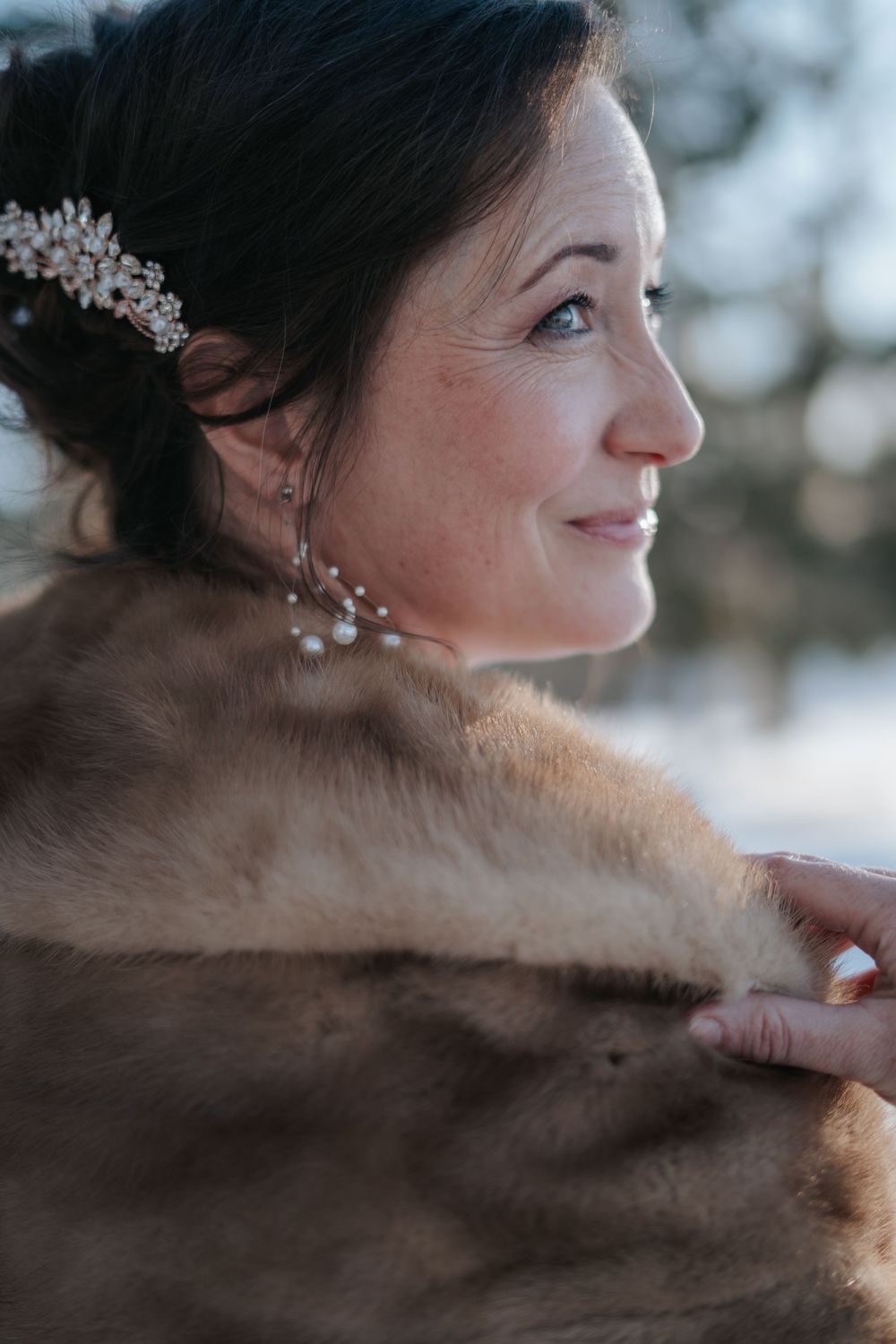 Profile view of bride wearing fur wrap and crystal hair accessory.