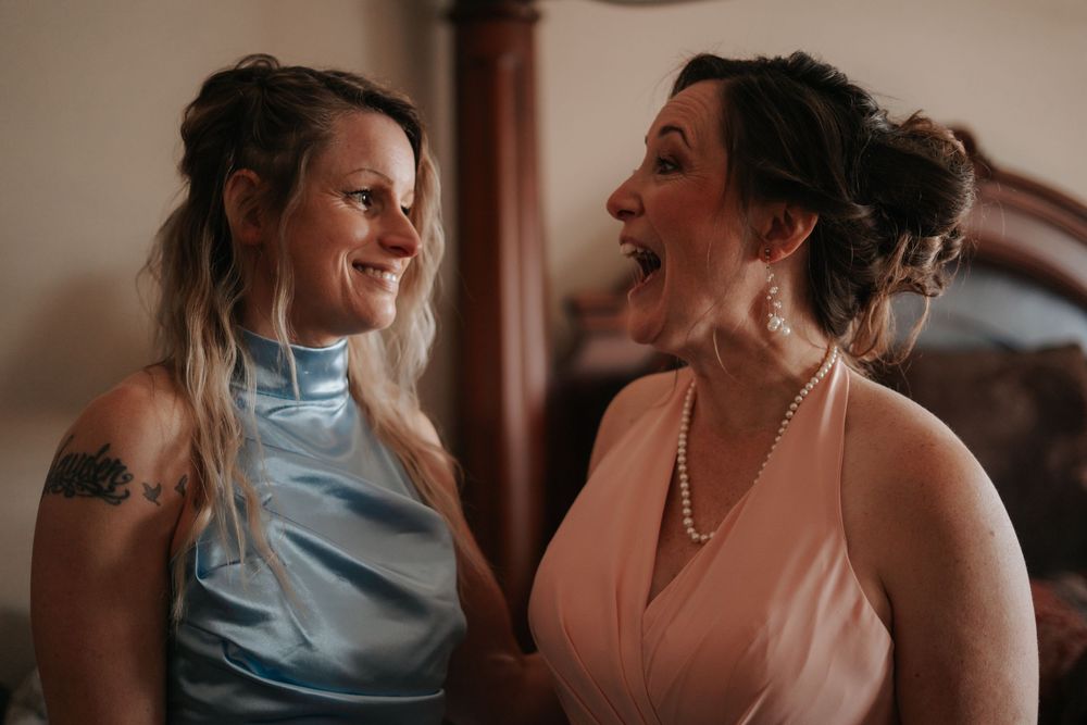 Two people in blue and peach dresses share a joyful moment indoors.