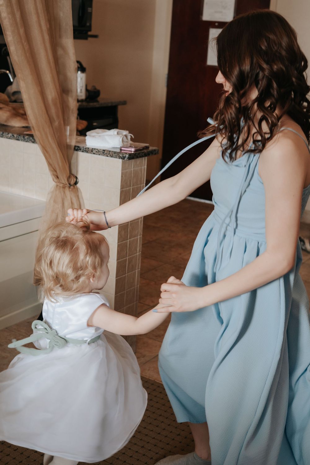 A person in a light blue dress holds hands with a small child in a white dress.