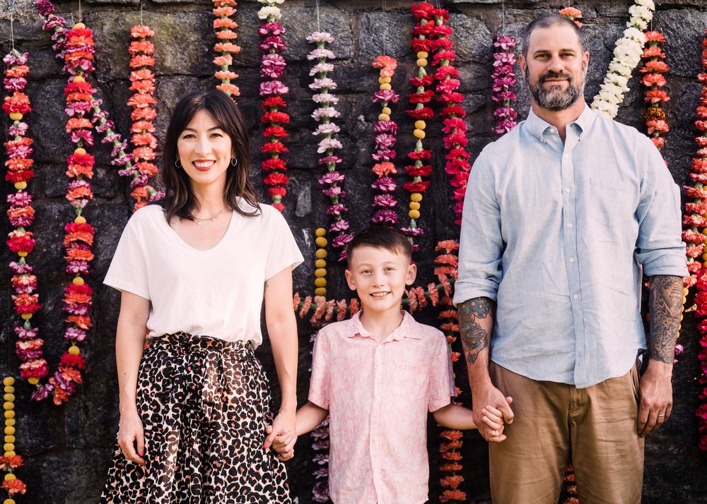 Family photo session against stone wall decorated with vibrant red and pink hanging flower strands.