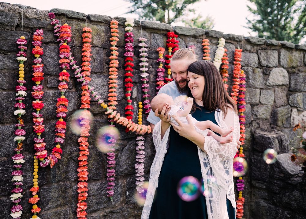 Outdoor family moment captured with bubbles and colorful hanging flower garlands against a stone wall.