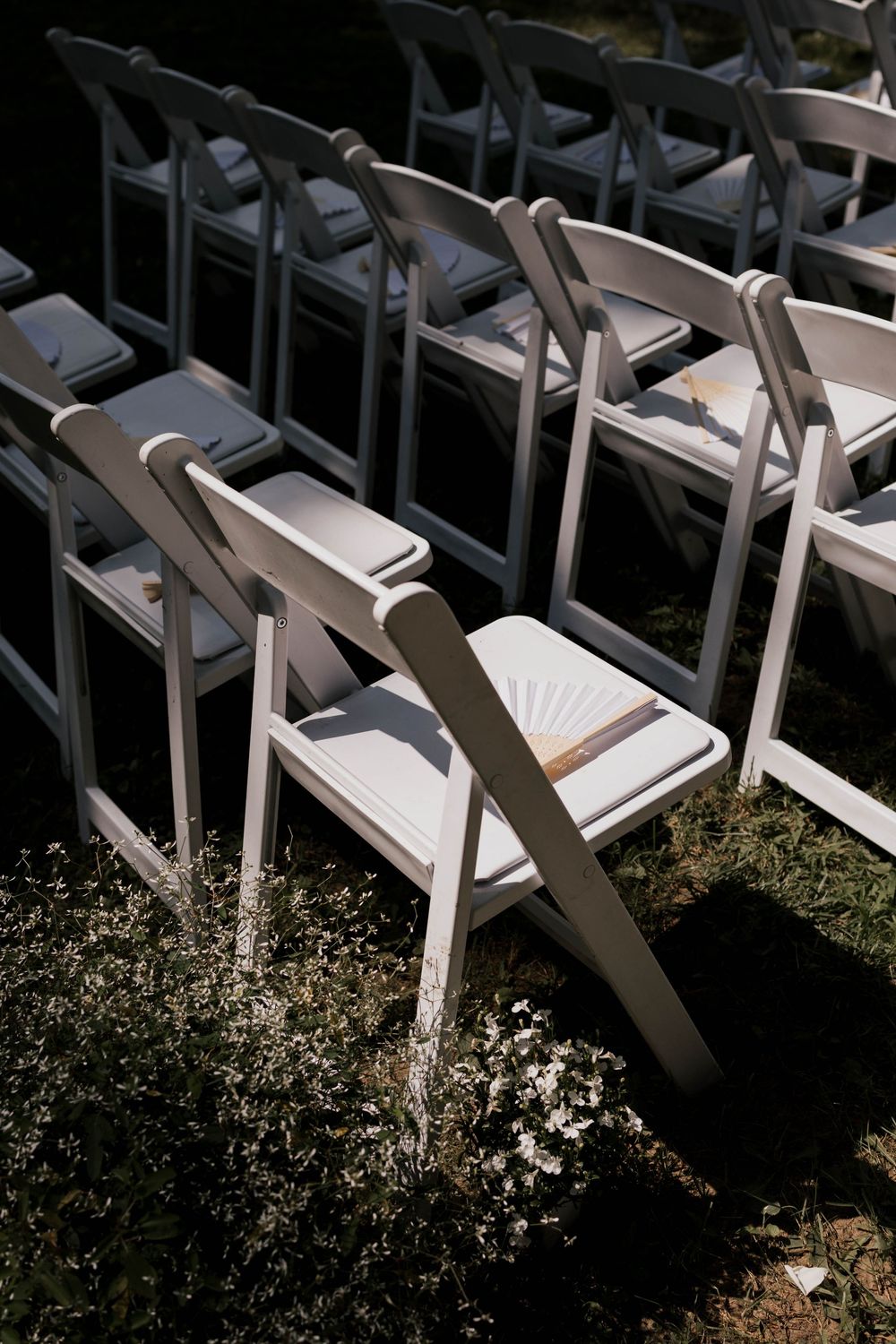 White wooden folding chairs with cushioned seats arranged in rows on grass for an outdoor wedding ceremony.