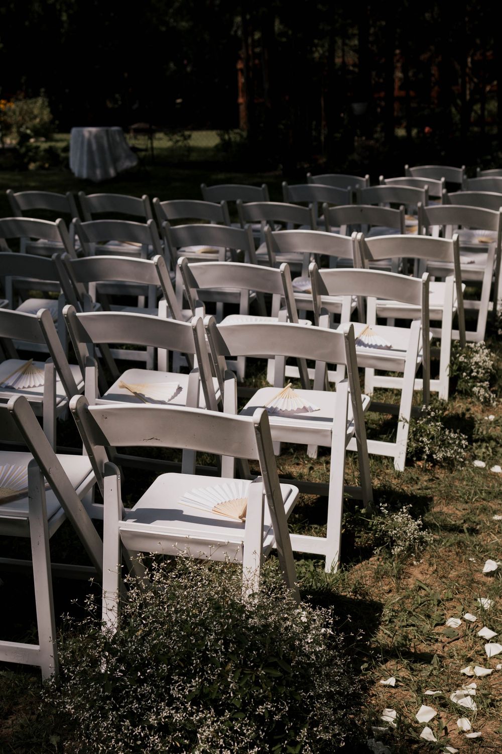 Rows of white folding chairs with programs set up for outdoor wedding ceremony.