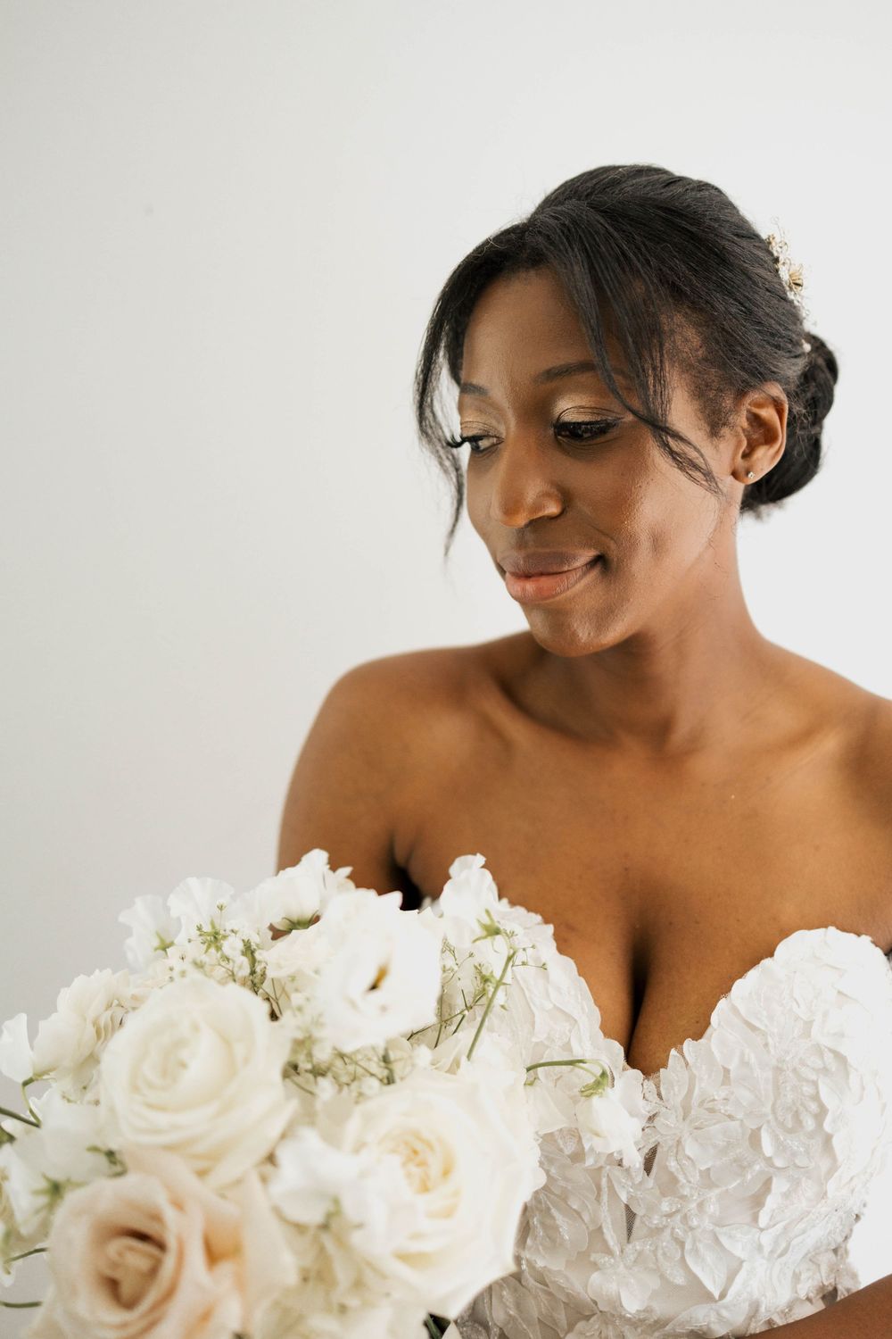 Elegant Black bride in a lace gown gazes down at her white rose and peony bridal bouquet.