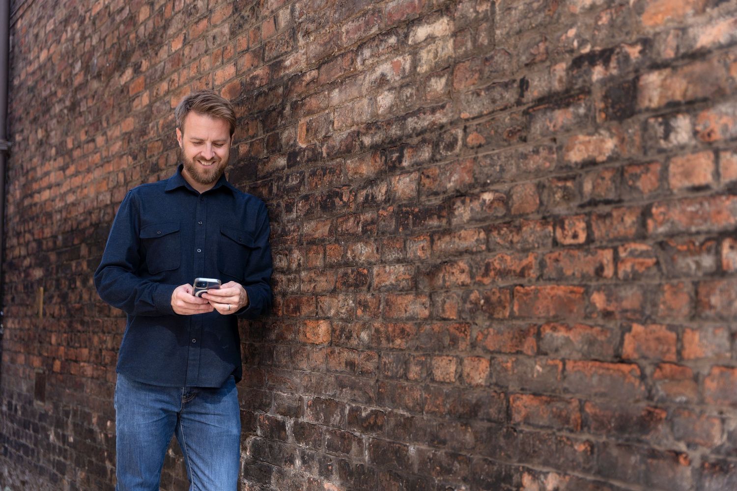 Life coach smiles while leaning against a railing on an outdoor balcony with brick buildings visible in the background.