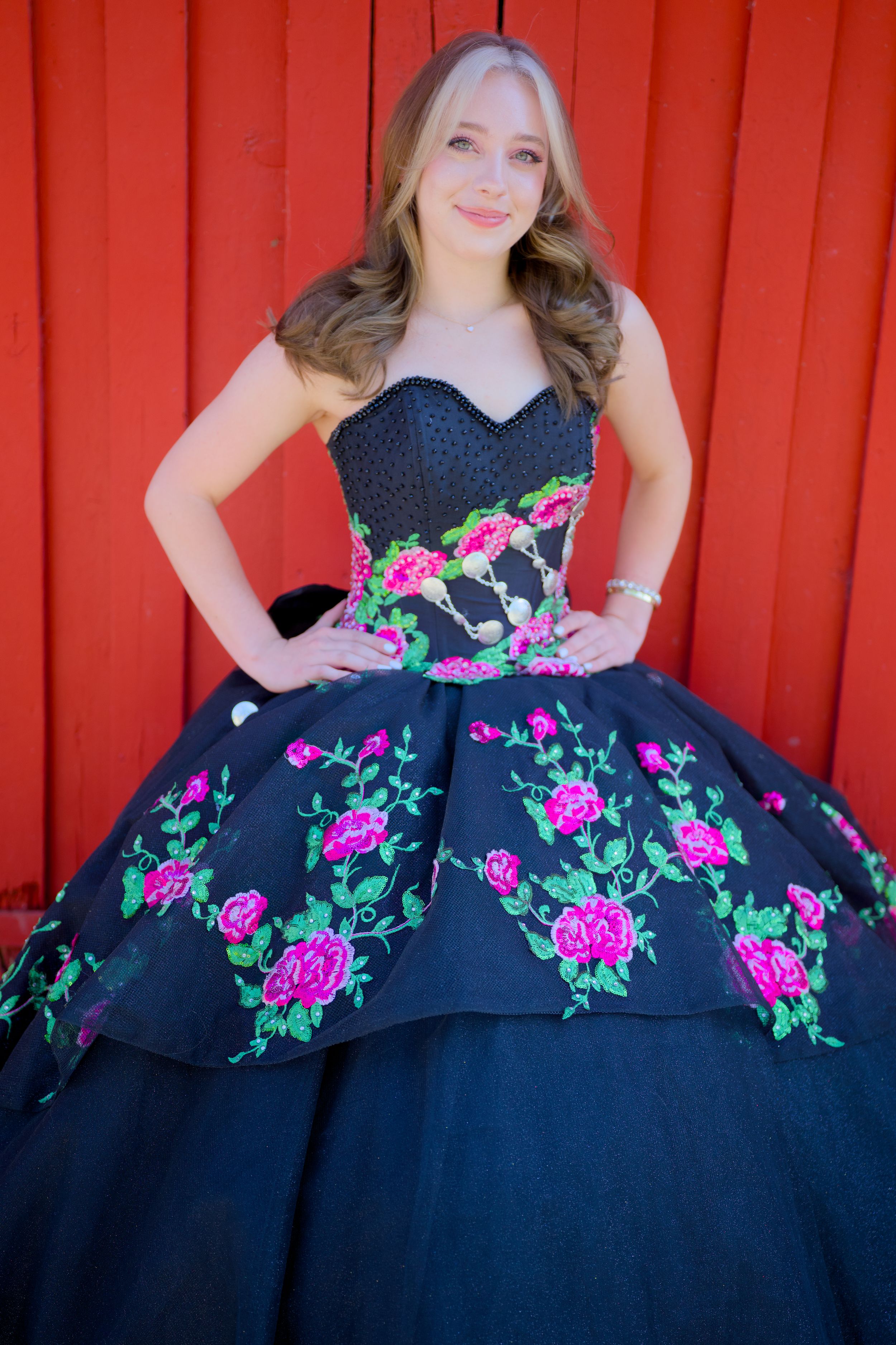 Stunning black ball gown with vibrant pink floral embroidery against a bright red backdrop.