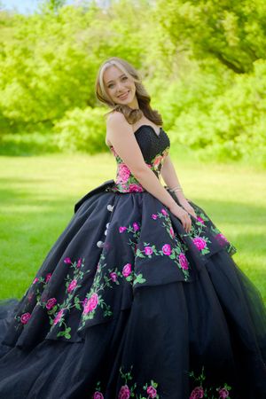 A black ballgown with vibrant pink floral embellishments photographed against lush green foliage in a garden setting.