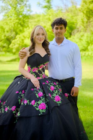 Couple posing for prom photos outdoors, with her wearing a black floral gown.