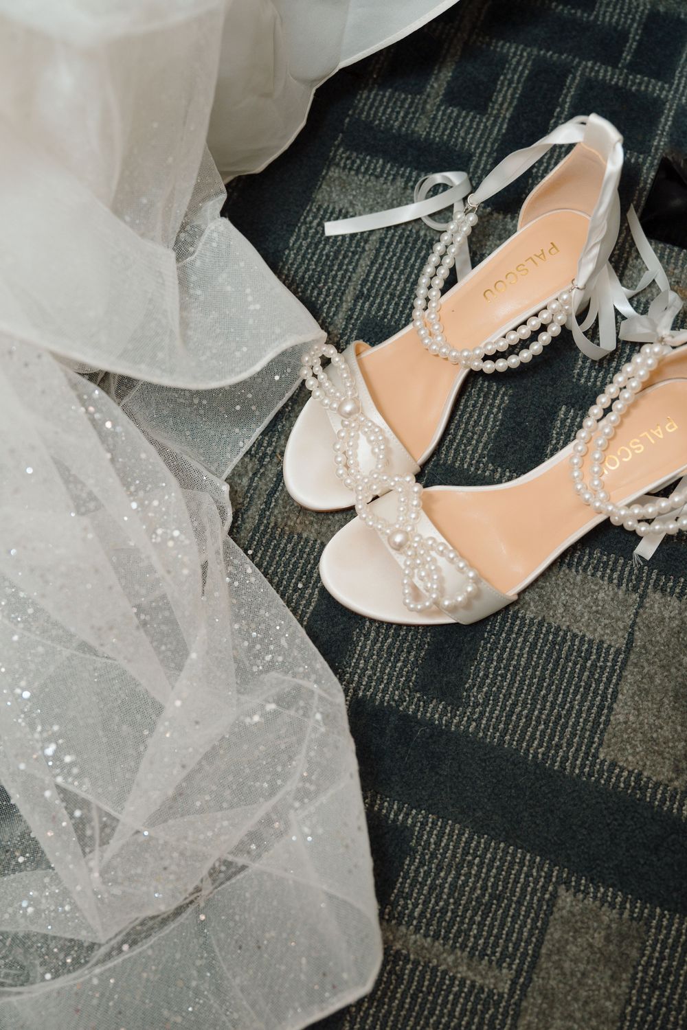 Elegant white bridal shoes with pearl embellishments lay beside delicate tulle fabric.