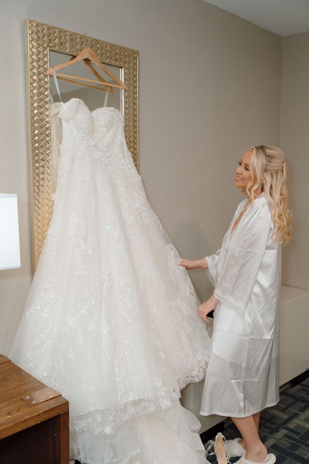 A white lace wedding dress hangs on display as someone in a robe admires it.