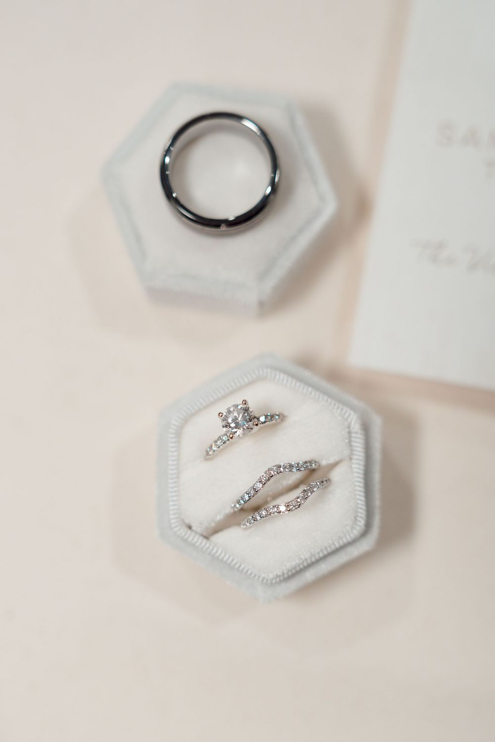 Wedding rings and engagement ring displayed in hexagonal white ring boxes.