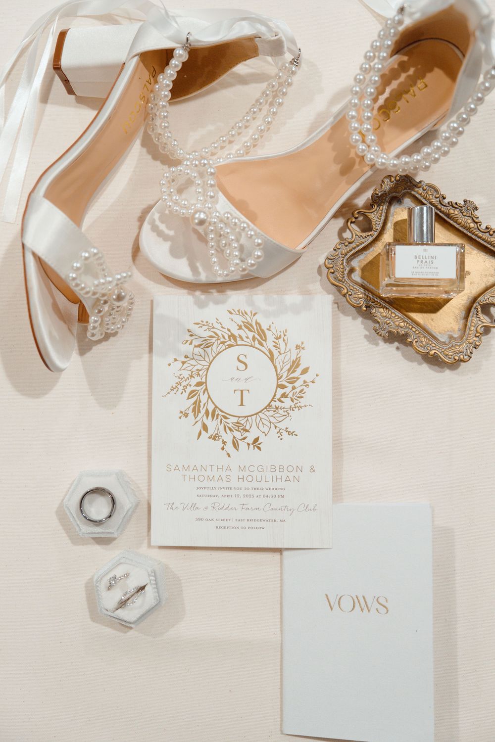 Elegant wedding invitation suite with vows booklet and crystal-embellished bridal shoes on marble background.