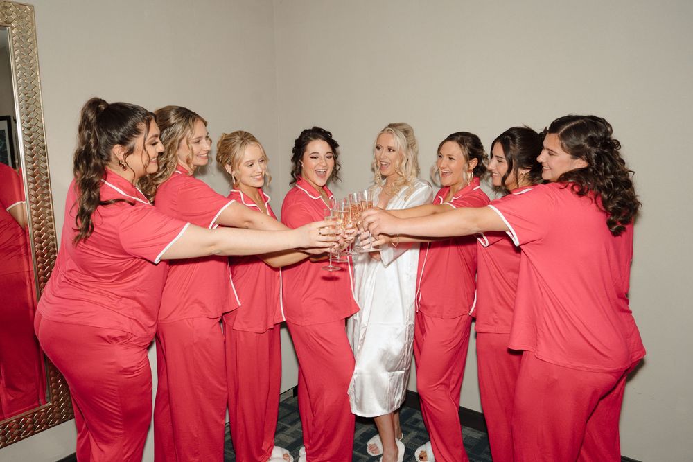 A group of bridesmaids in matching coral scrubs join hands in celebration before a wedding ceremony.