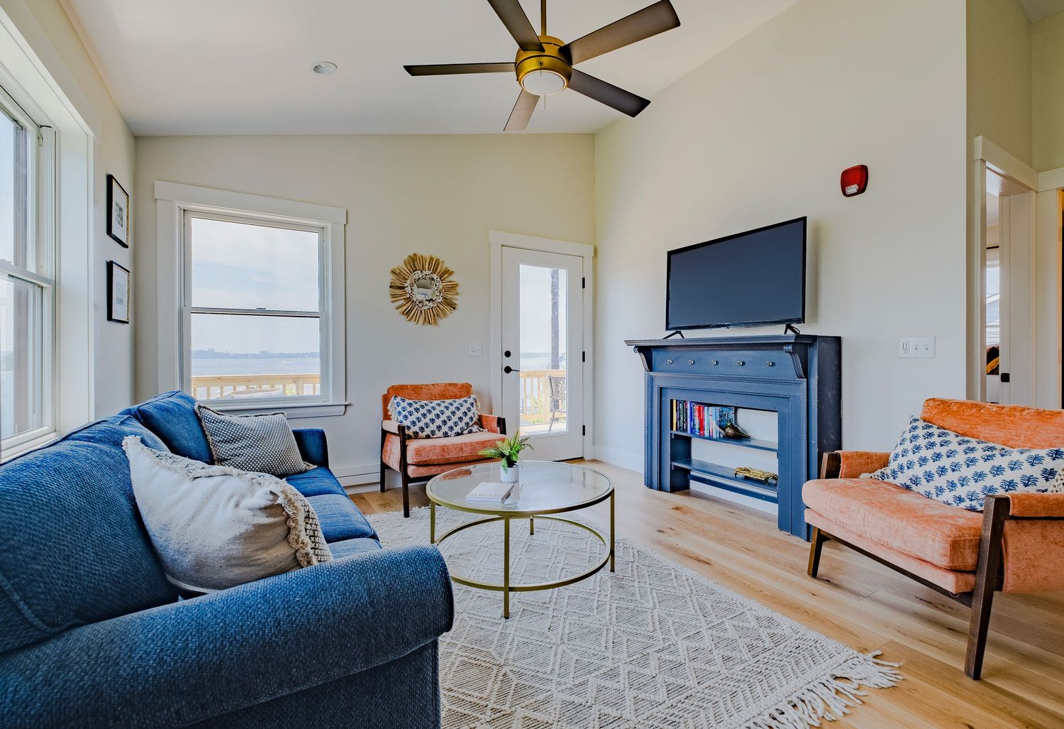 Modern living room with navy blue couch, brown leather chairs, mounted TV above fireplace, and geometric area rug.