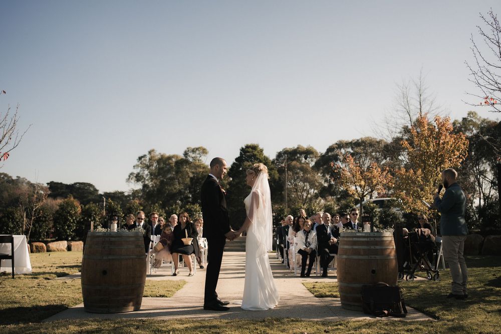 A wedding party poses between rustic wine barrels at an outdoor vineyard ceremony during golden hour.