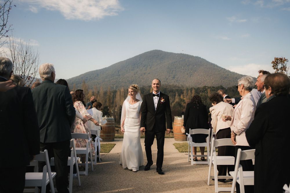 A wedding ceremony takes place outdoors with a majestic mountain peak rising in the background under blue skies.