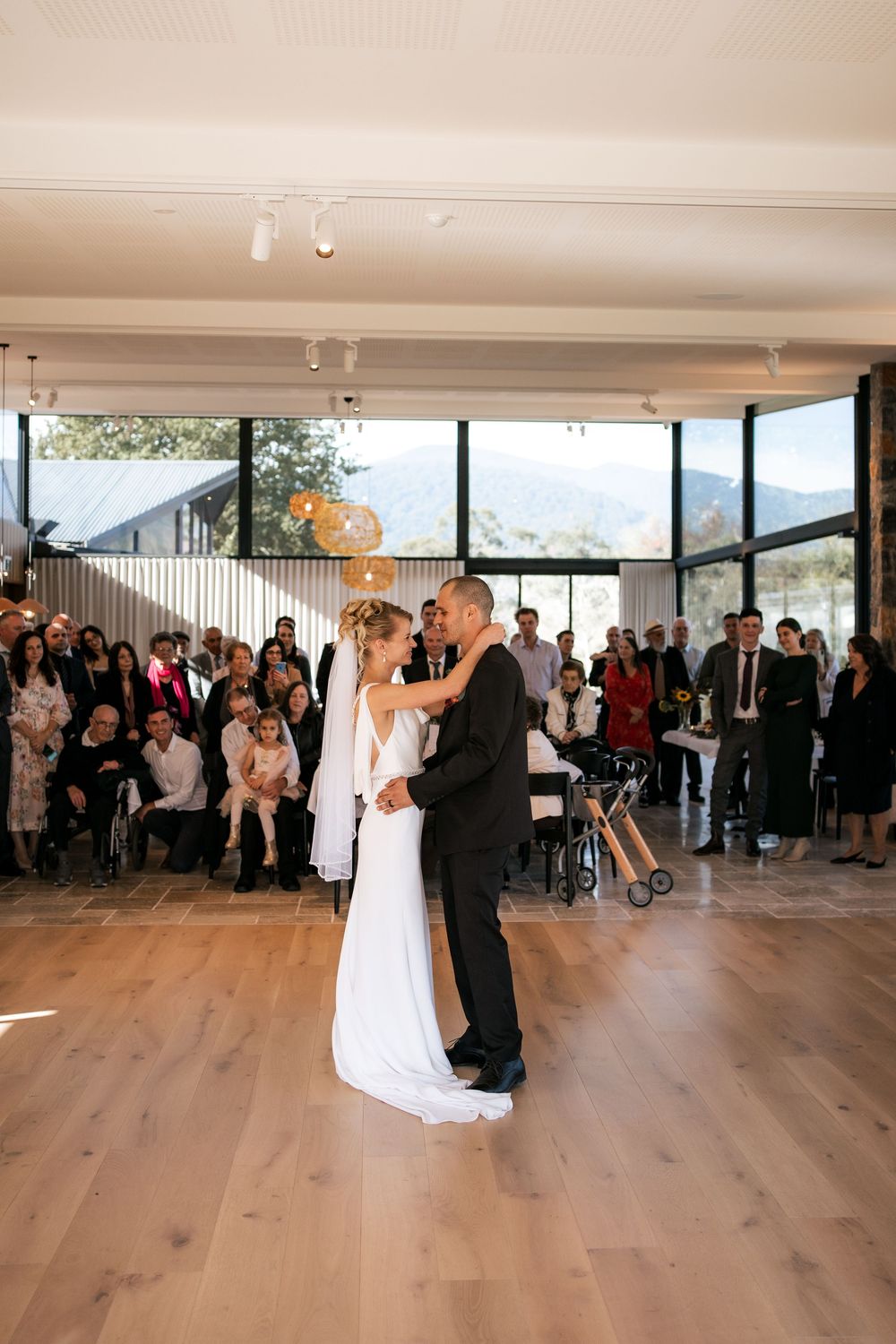 Couple shares their first dance in a modern venue with mountain views and gathered guests.