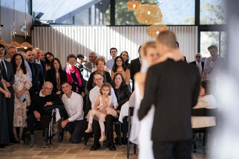 Wedding guests gathered to watch speeches during an indoor reception ceremony.