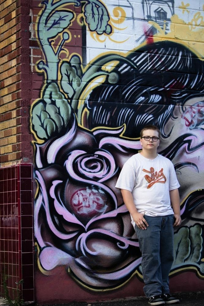 A young man stands by a wall of colorful graffiti art while posing for a photo.