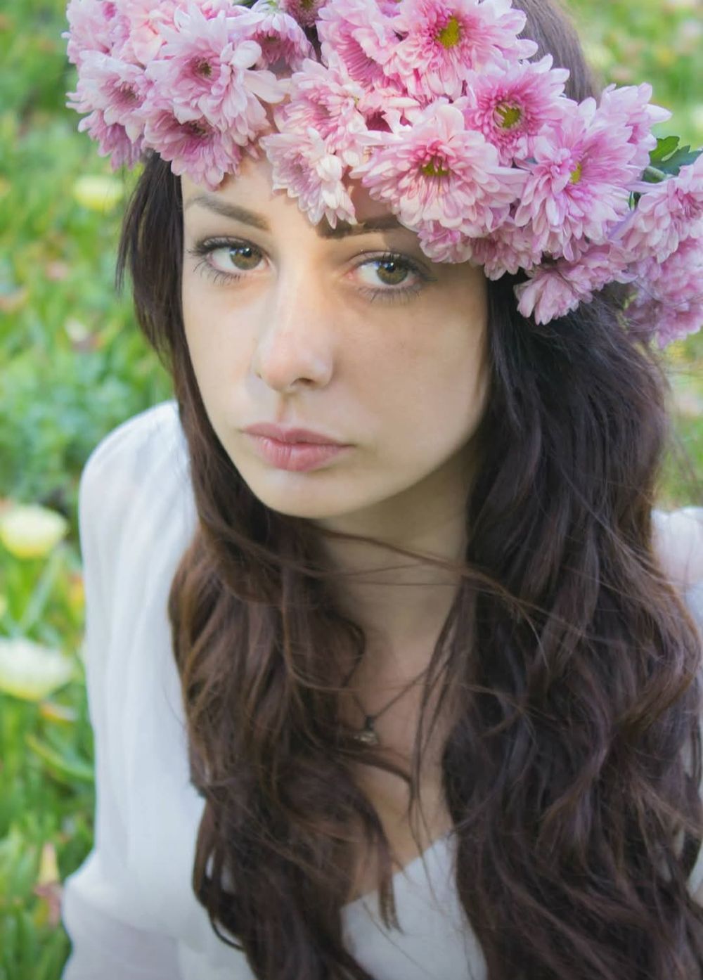 A young woman wearing a crown of flowers poses near a field of flowers.
