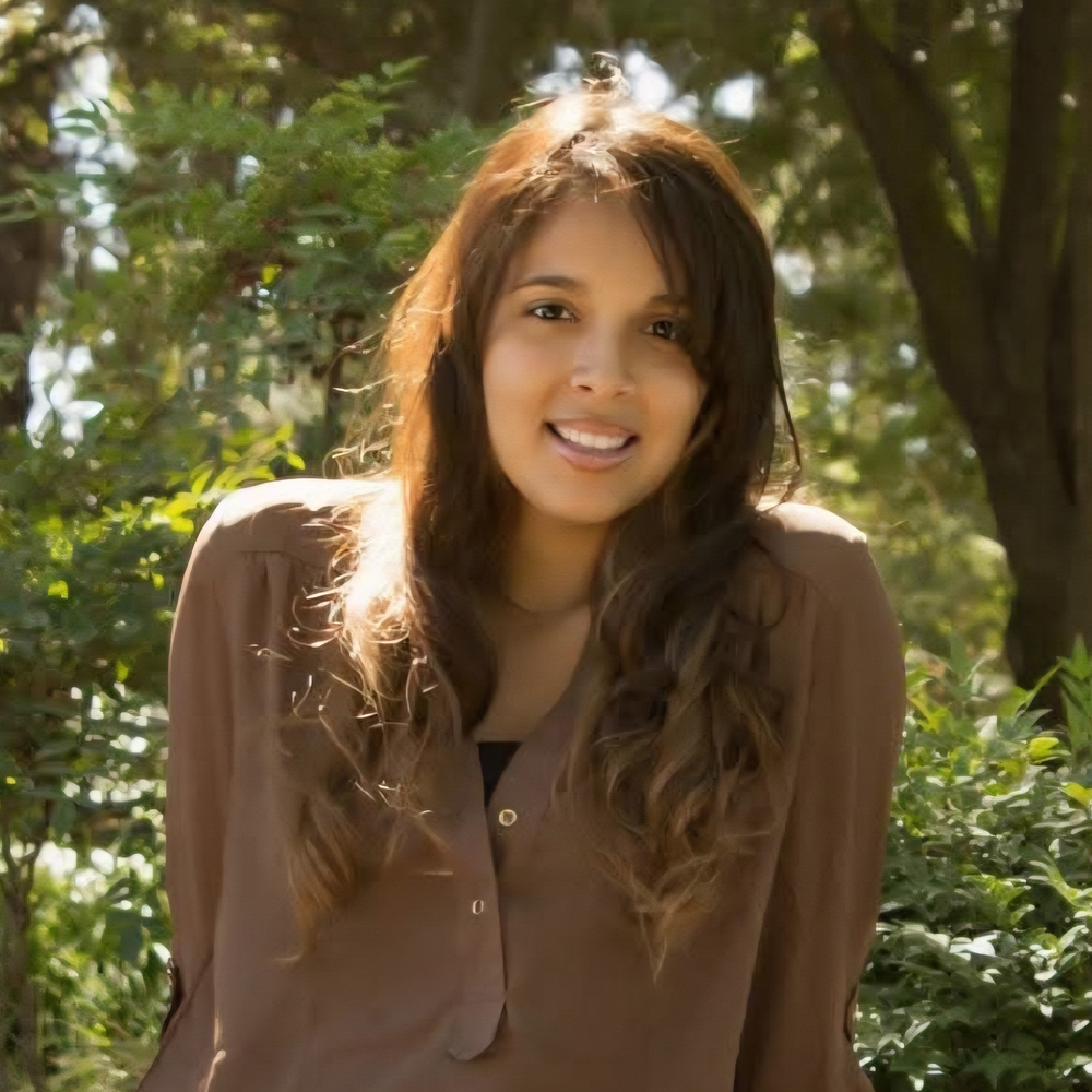 A young woman poses for a senior photo while outdoors in a park.