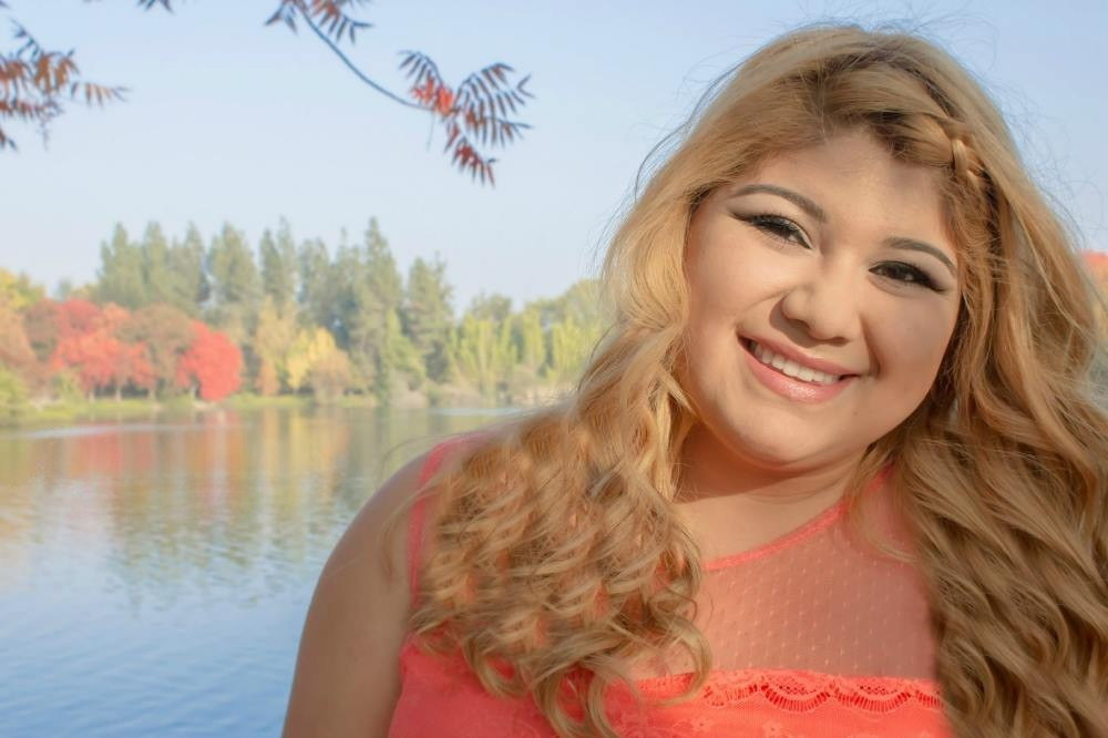 A young woman poses for a senior photo while outdoors by a lake with fall colors.